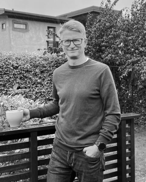 Knut Martin Tornes outdoors by a garden fence, holding a cup of coffee
